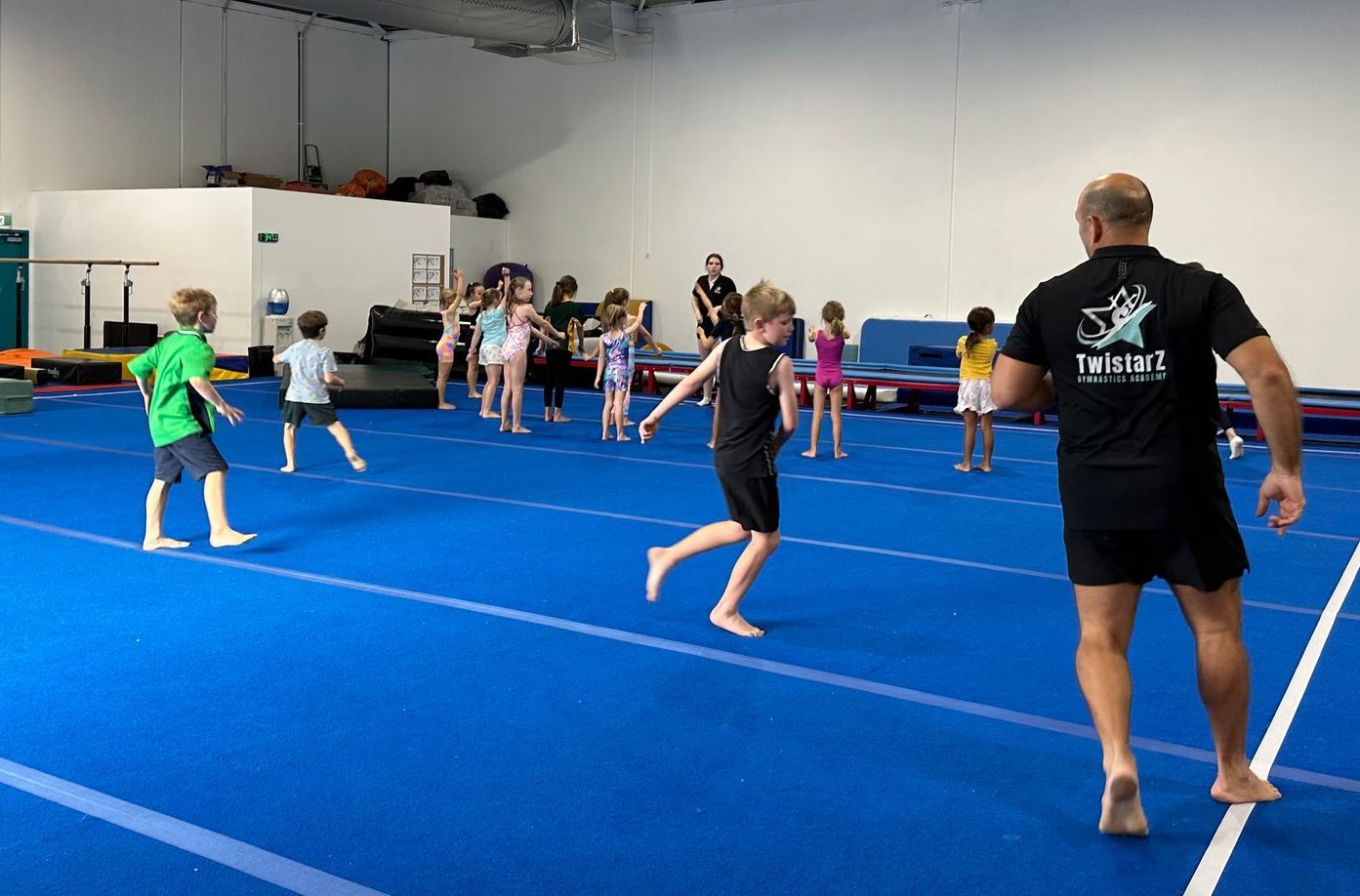 A group of children are playing on a blue mat in a gym.