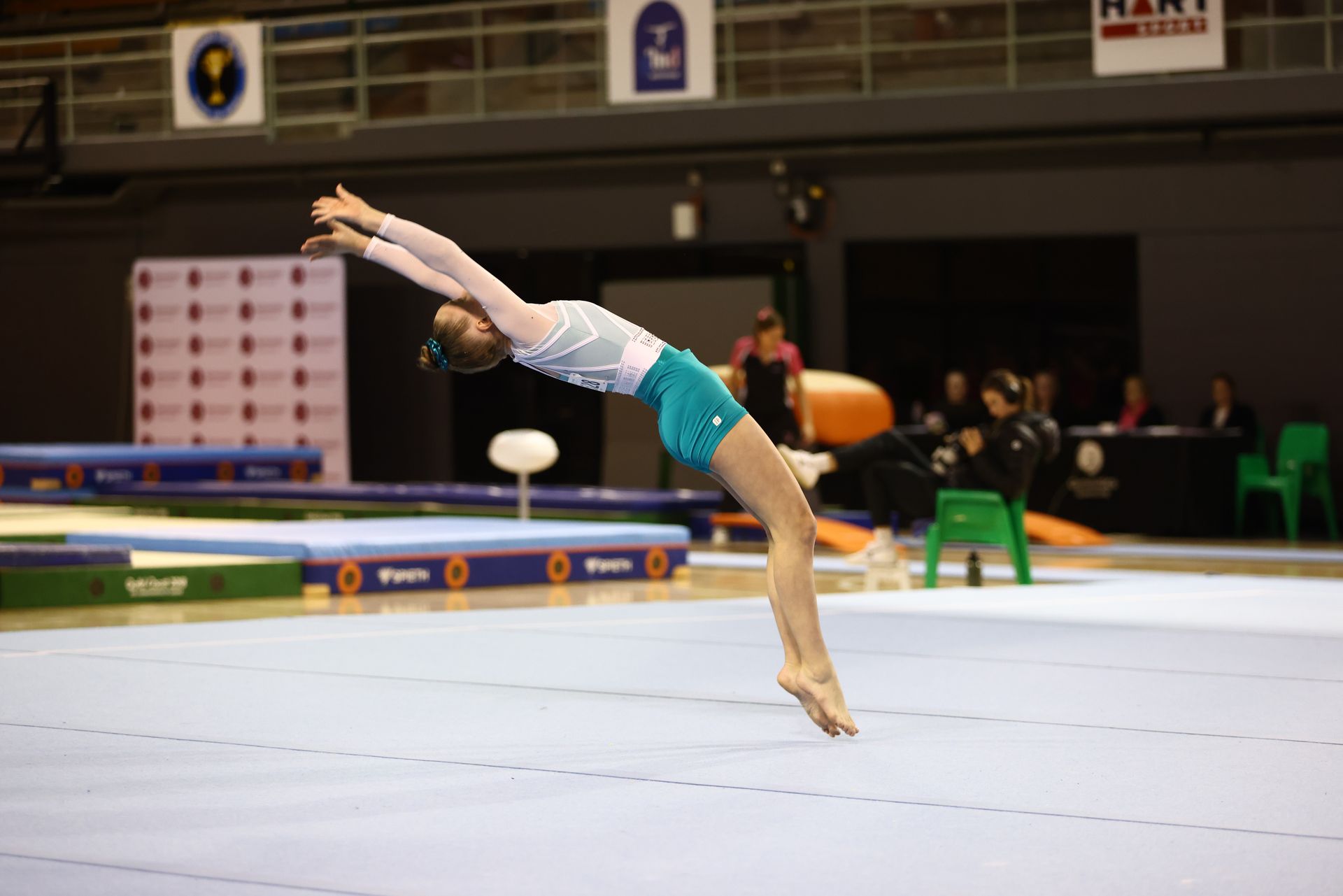 A female gymnast is doing a flik on a mat in a gym.