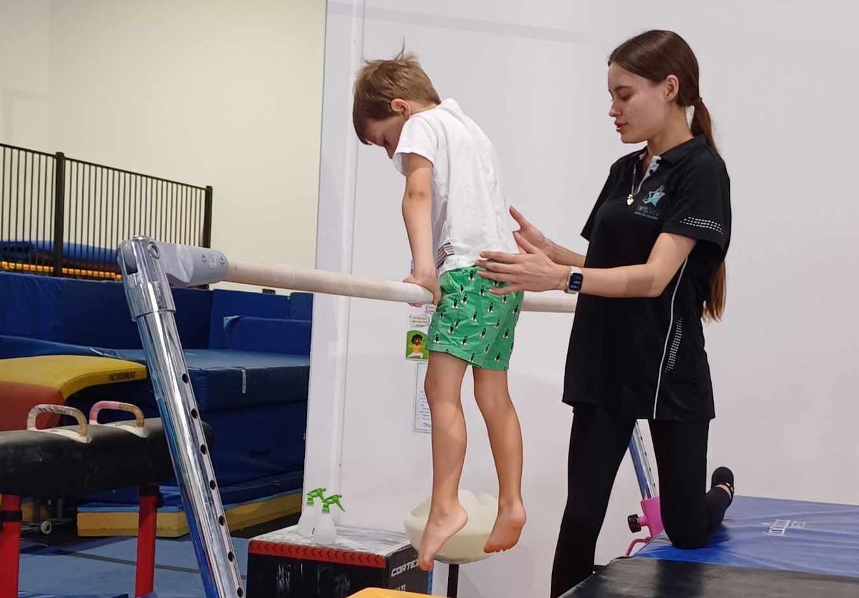 A coach is helping a young boy balance on a bar.