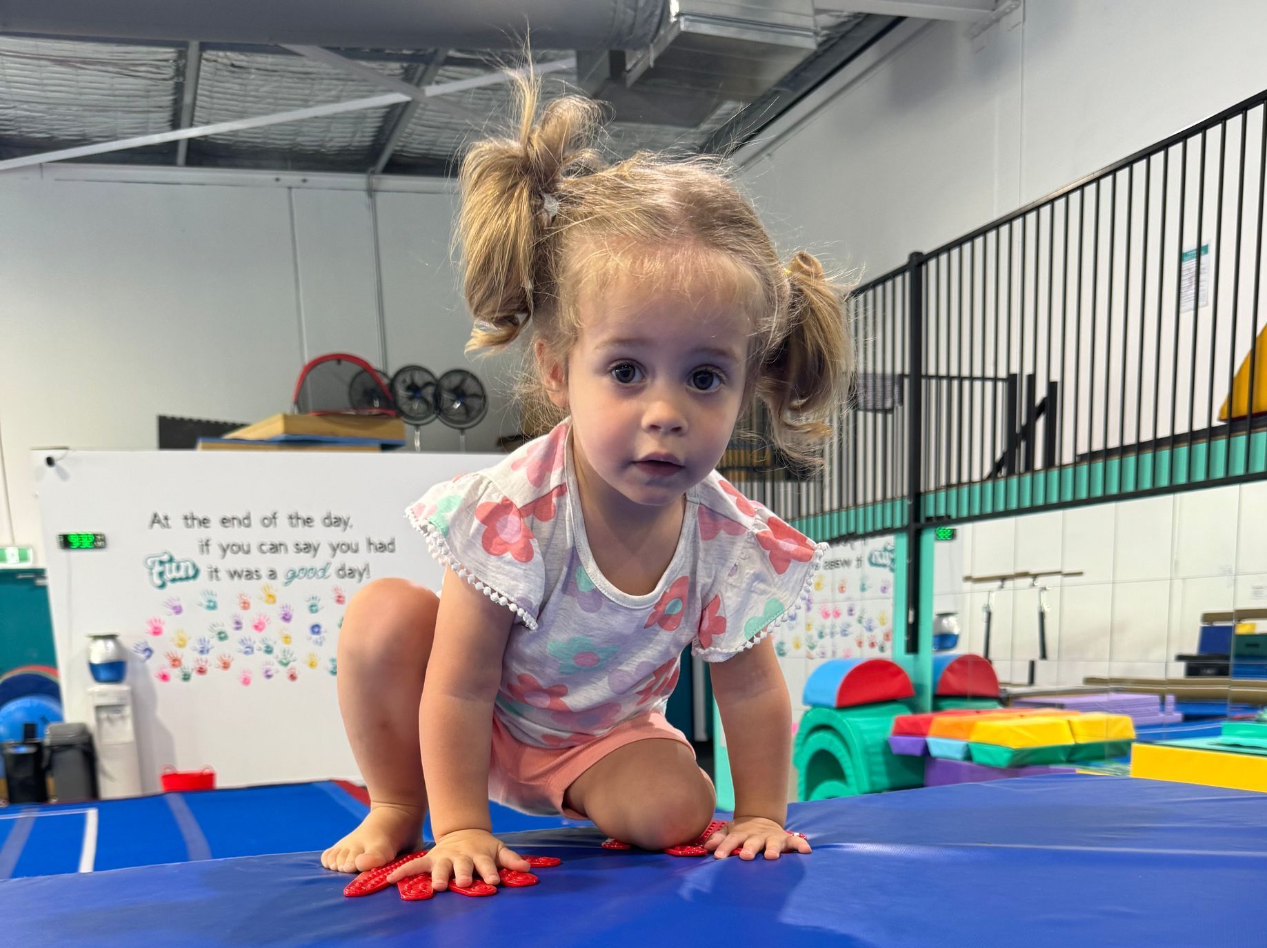 A little girl is crawling on a blue mat in a gym.