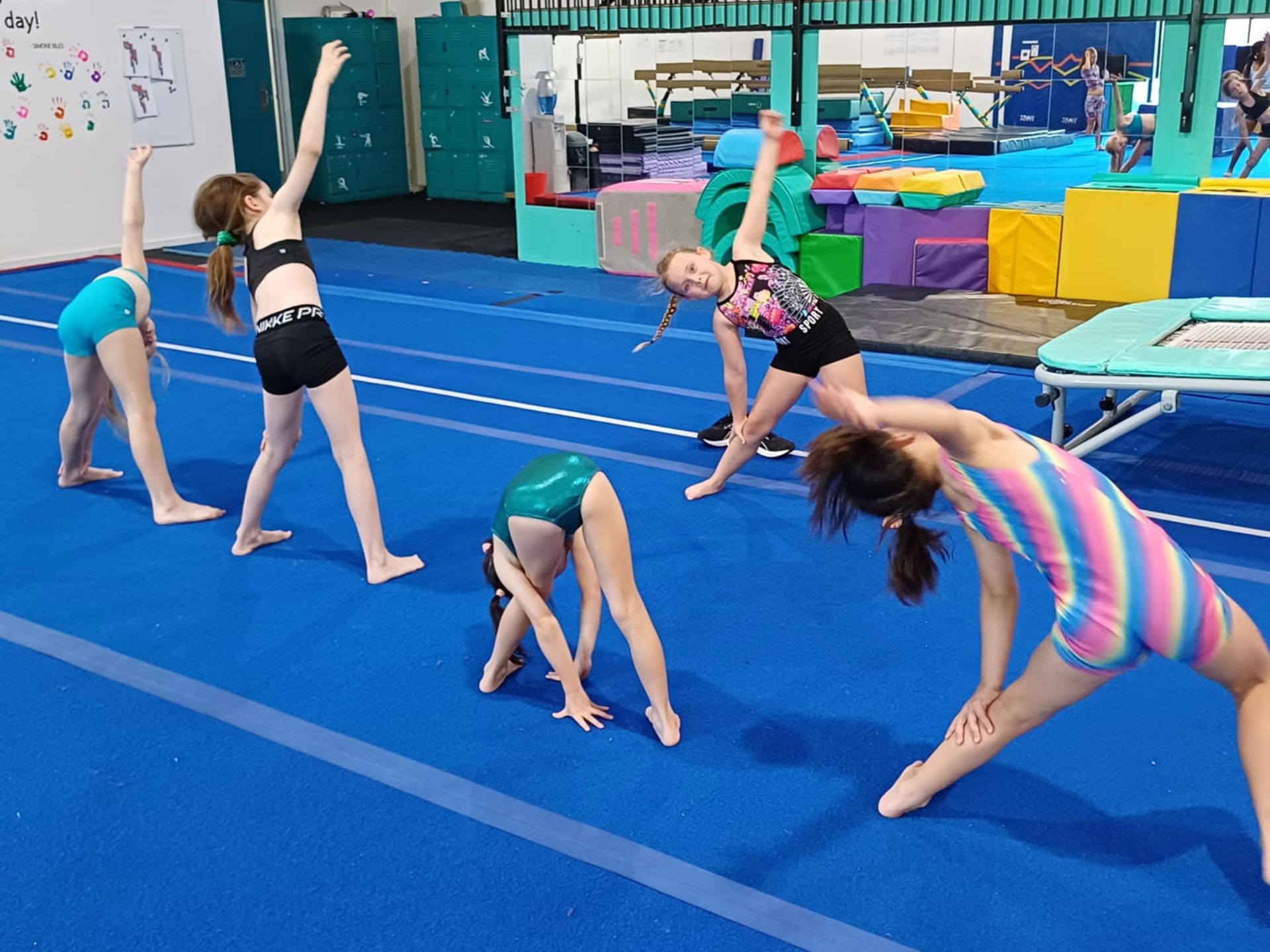 A group of young girls are doing gymnastics on a blue mat in a gym.