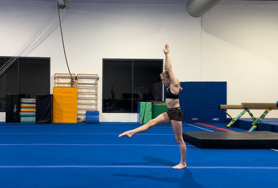 A woman is doing a split on a blue mat in a gym.