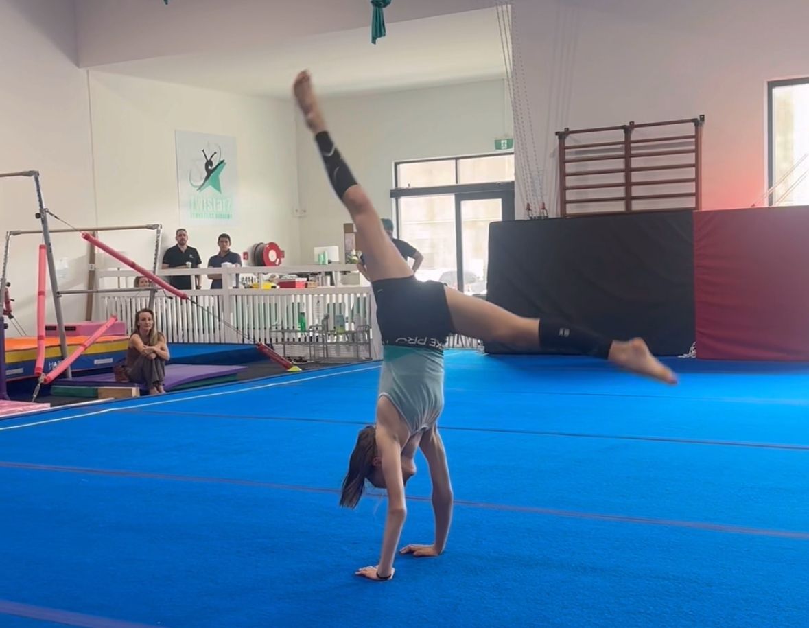 A girl is doing a handstand on a blue mat in a gym.