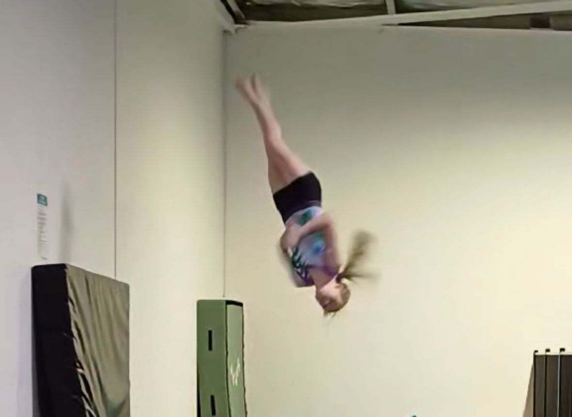 A woman is doing a tumble into a pit in a gym.
