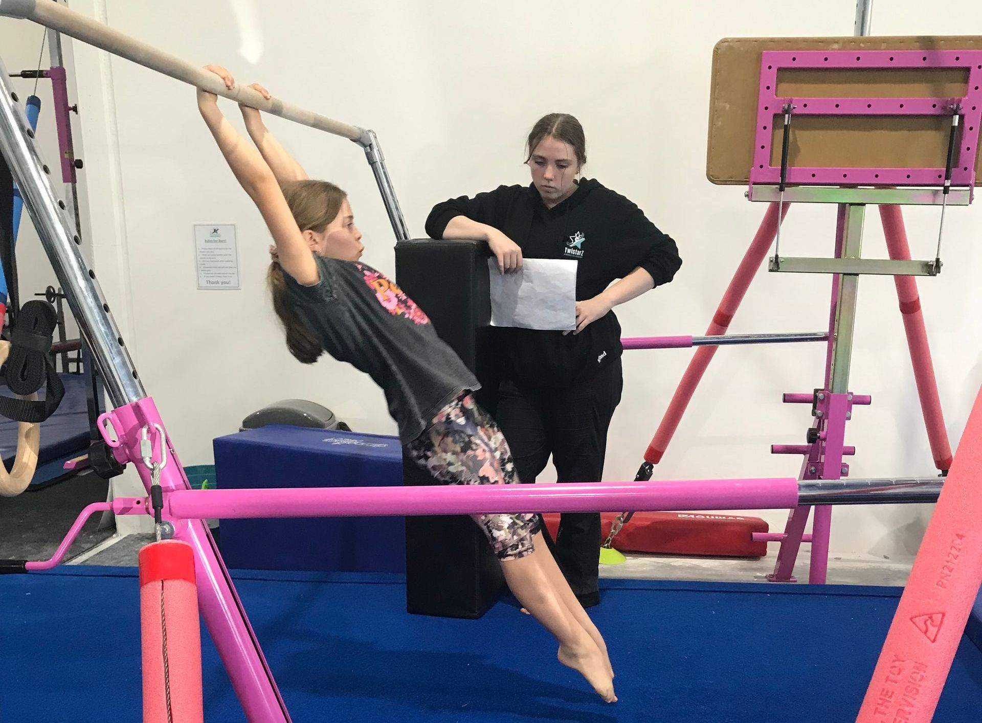 A girl is doing a handstand on a balance beam while a woman watches.