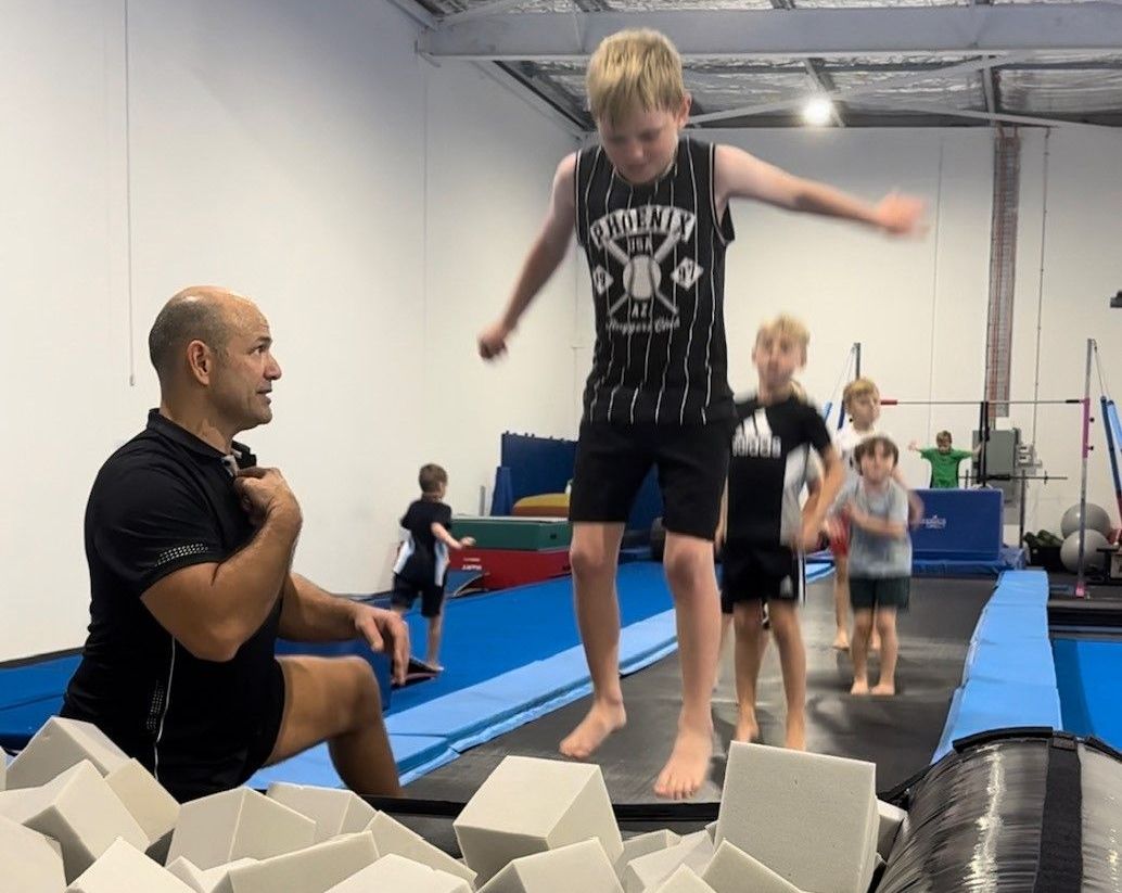 A young boy is jumping on a trampoline while coach watches.