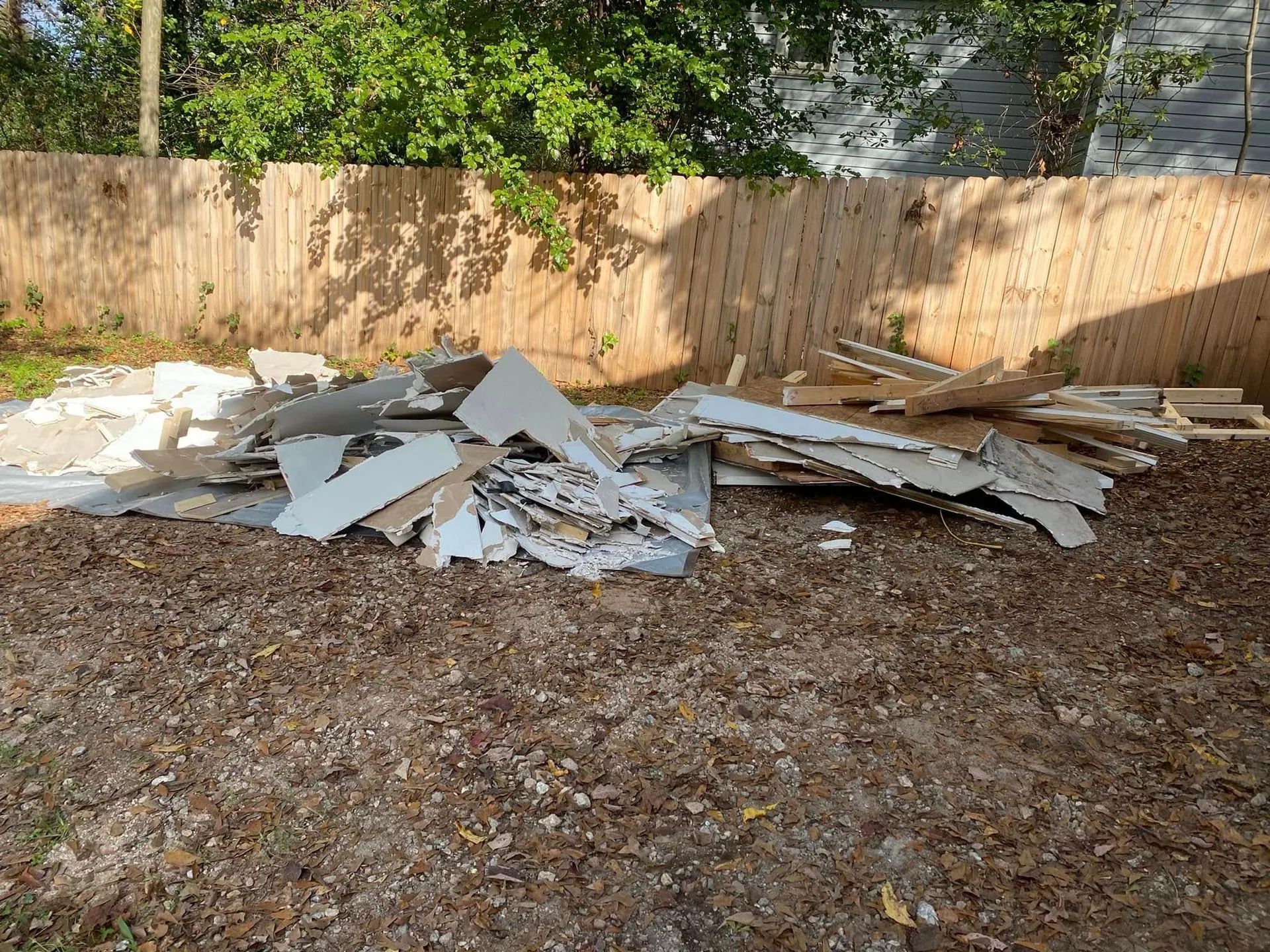 Pile of construction debris in a grassy backyard, in front of a wooden fence.