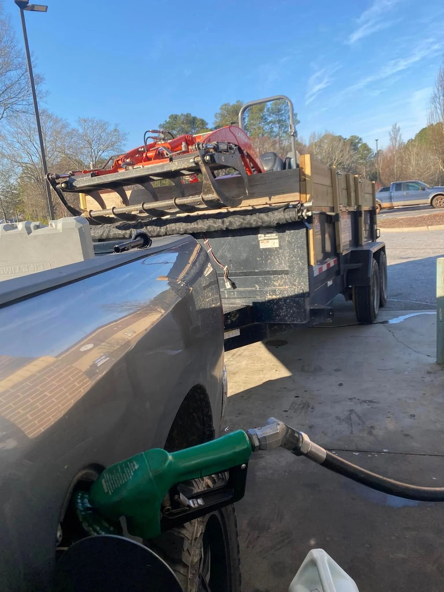 A vehicle refueling at a gas pump, towing a loaded trailer in a parking lot on a sunny day.