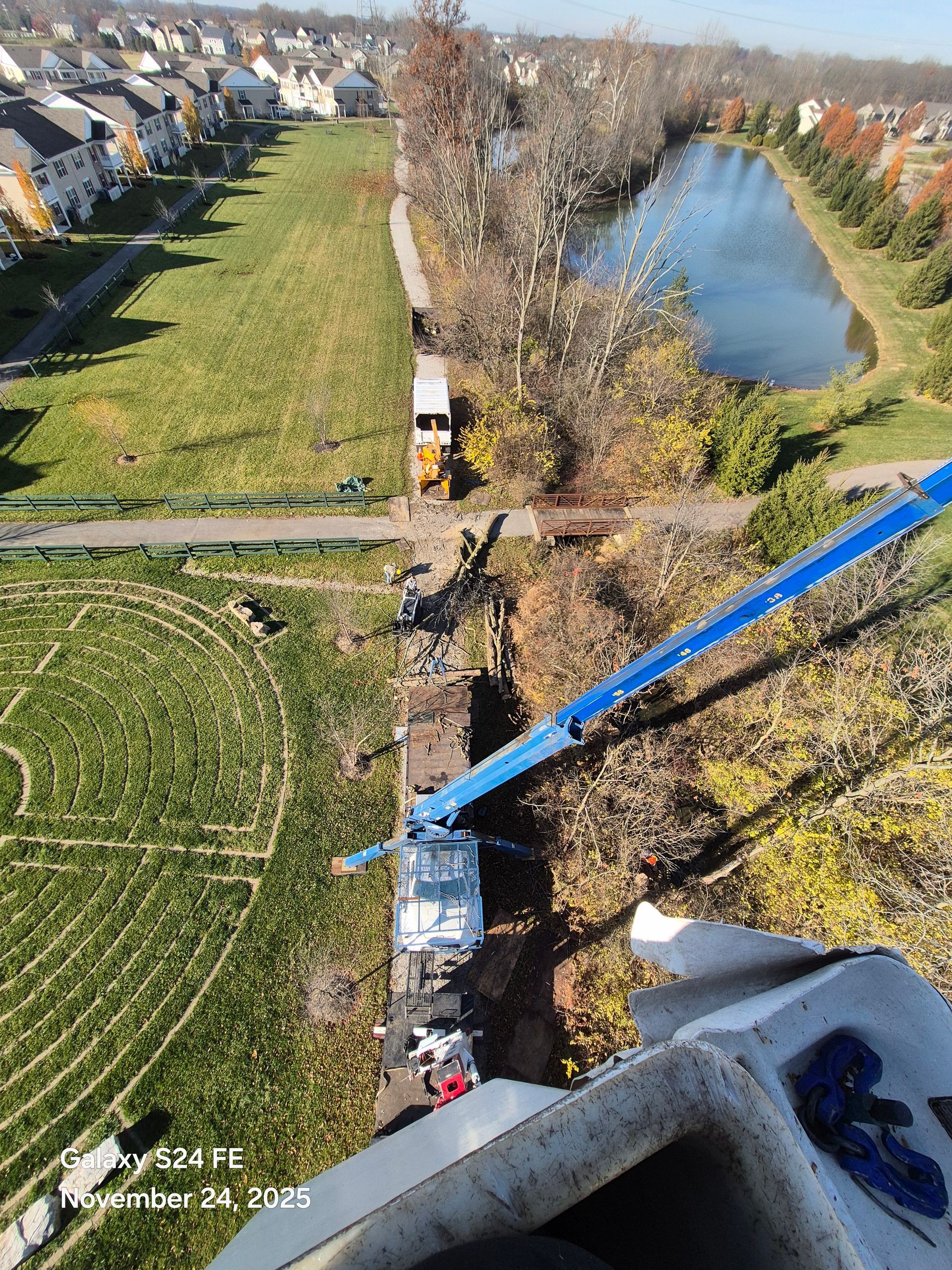 An aerial view shows a lift truck near a pond and green field with a residential area in the background.