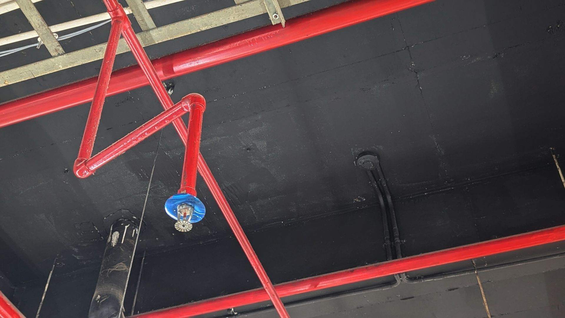 Red overhead pipes and a blue sprinkler valve on a dark industrial ceiling