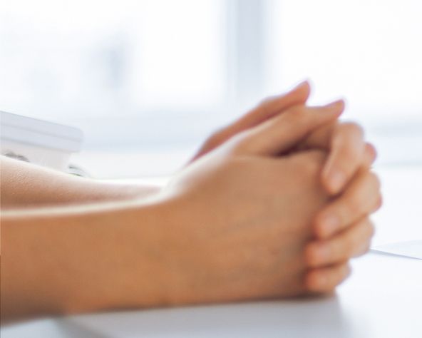 A woman is sitting at a table with her hands folded in prayer .