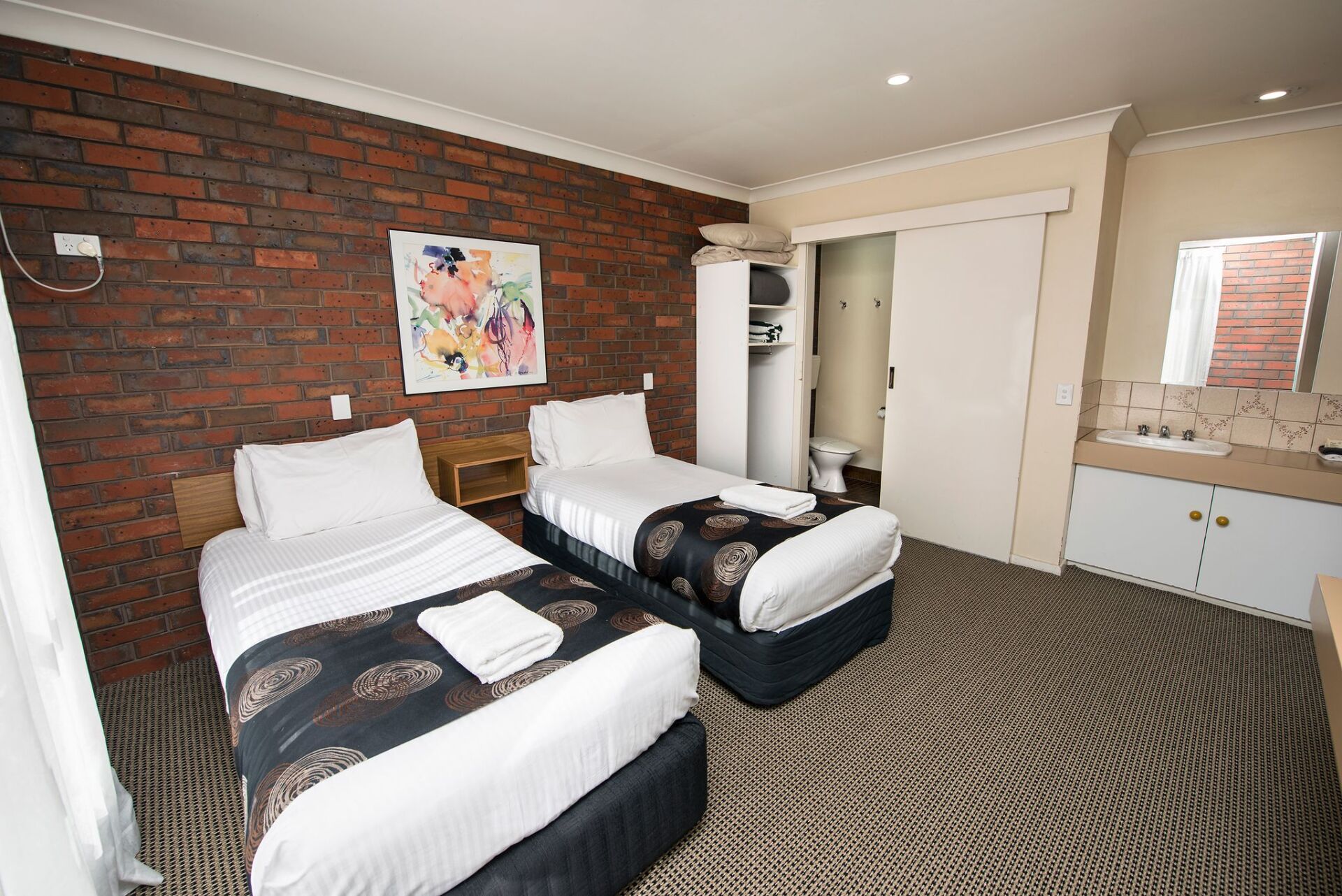 A motel room with two twin beds, a brick wall, and a bathroom.