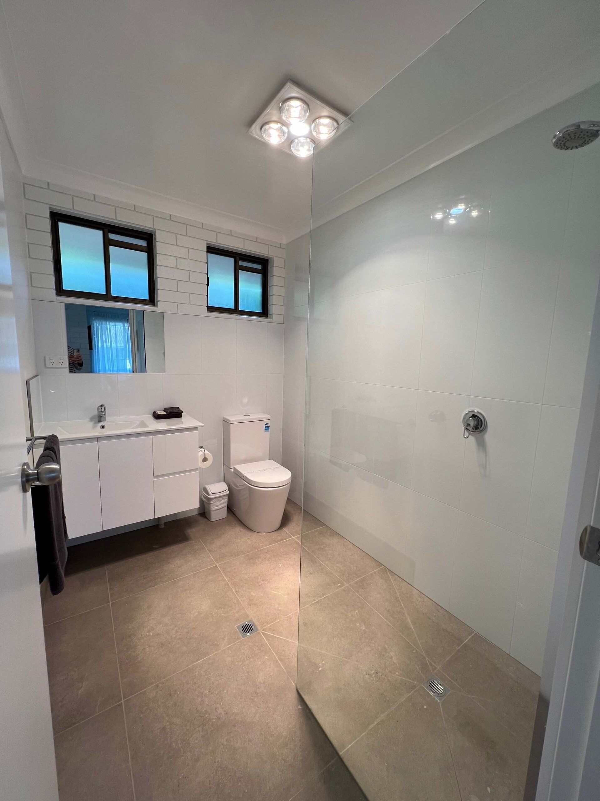 Modern bathroom with white walls, tiled floor, glass shower, toilet, and vanity.