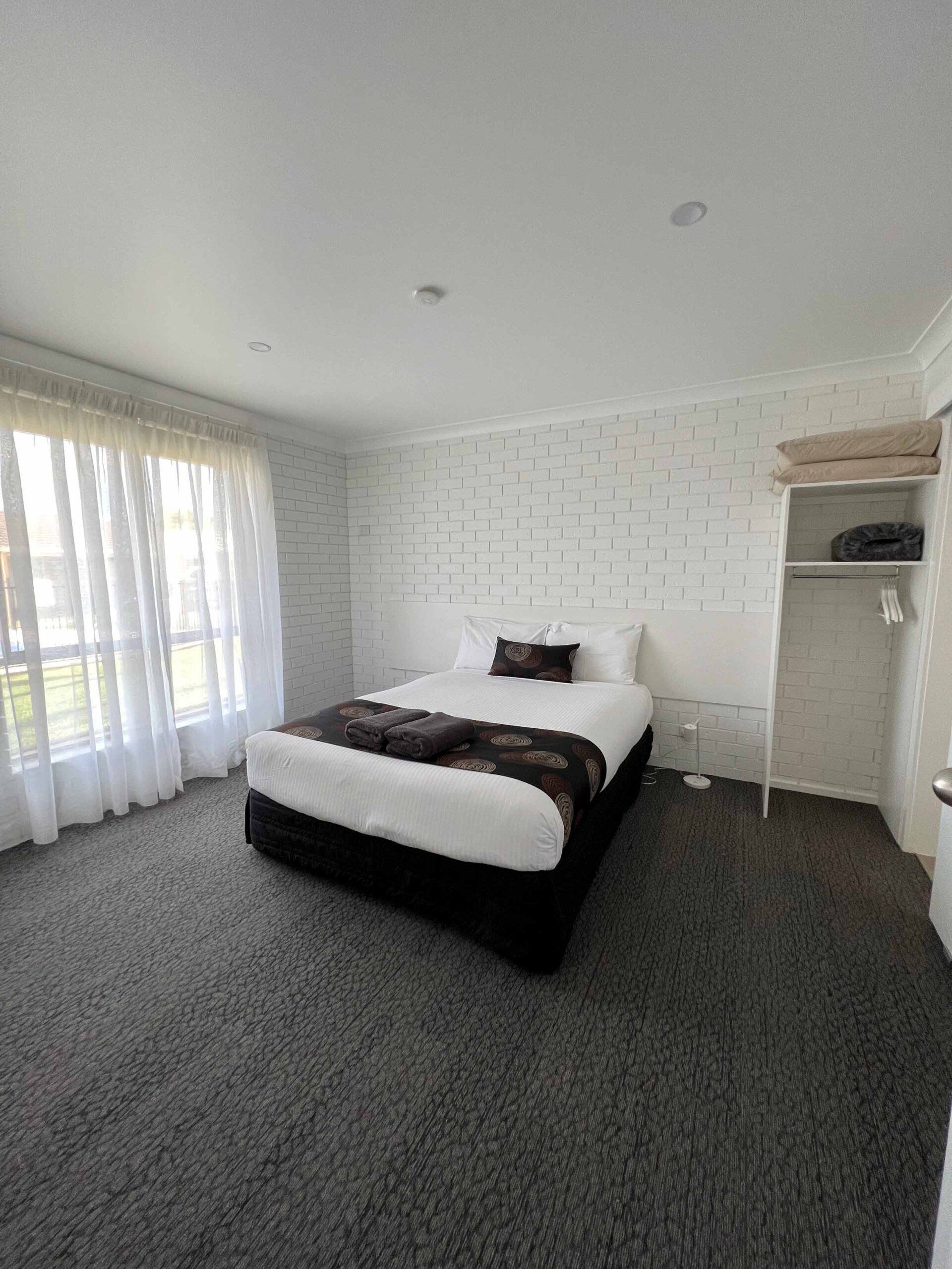 Bedroom with a bed, window with curtains, closet, and carpet. White walls, bedspread with brown accents.