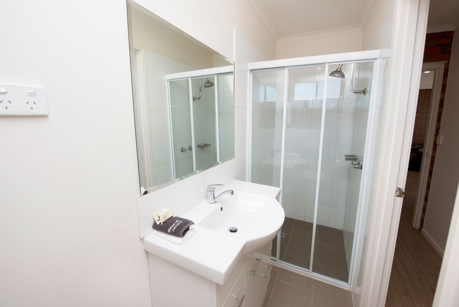 Bathroom with white sink, shower, and mirror; an open door leads to another room.