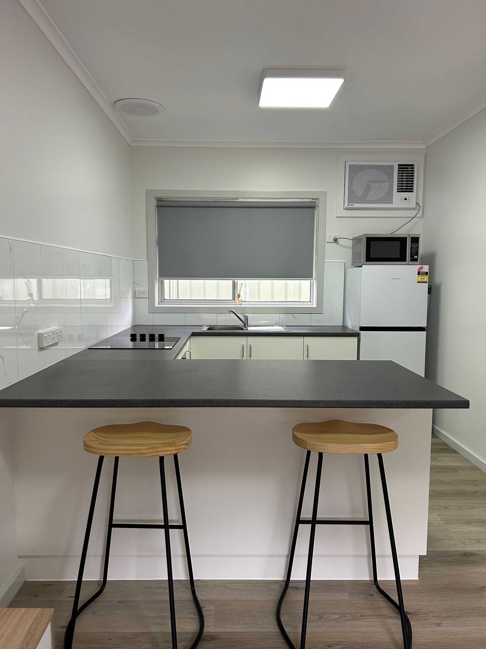 Modern kitchen with a breakfast bar, two stools, appliances, and a window.