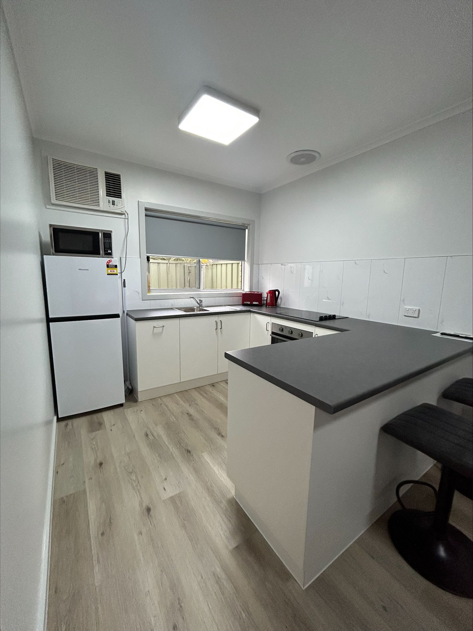 Modern kitchen with white cabinets, gray countertop, and light wood flooring. A refrigerator, stove, and sink are visible.