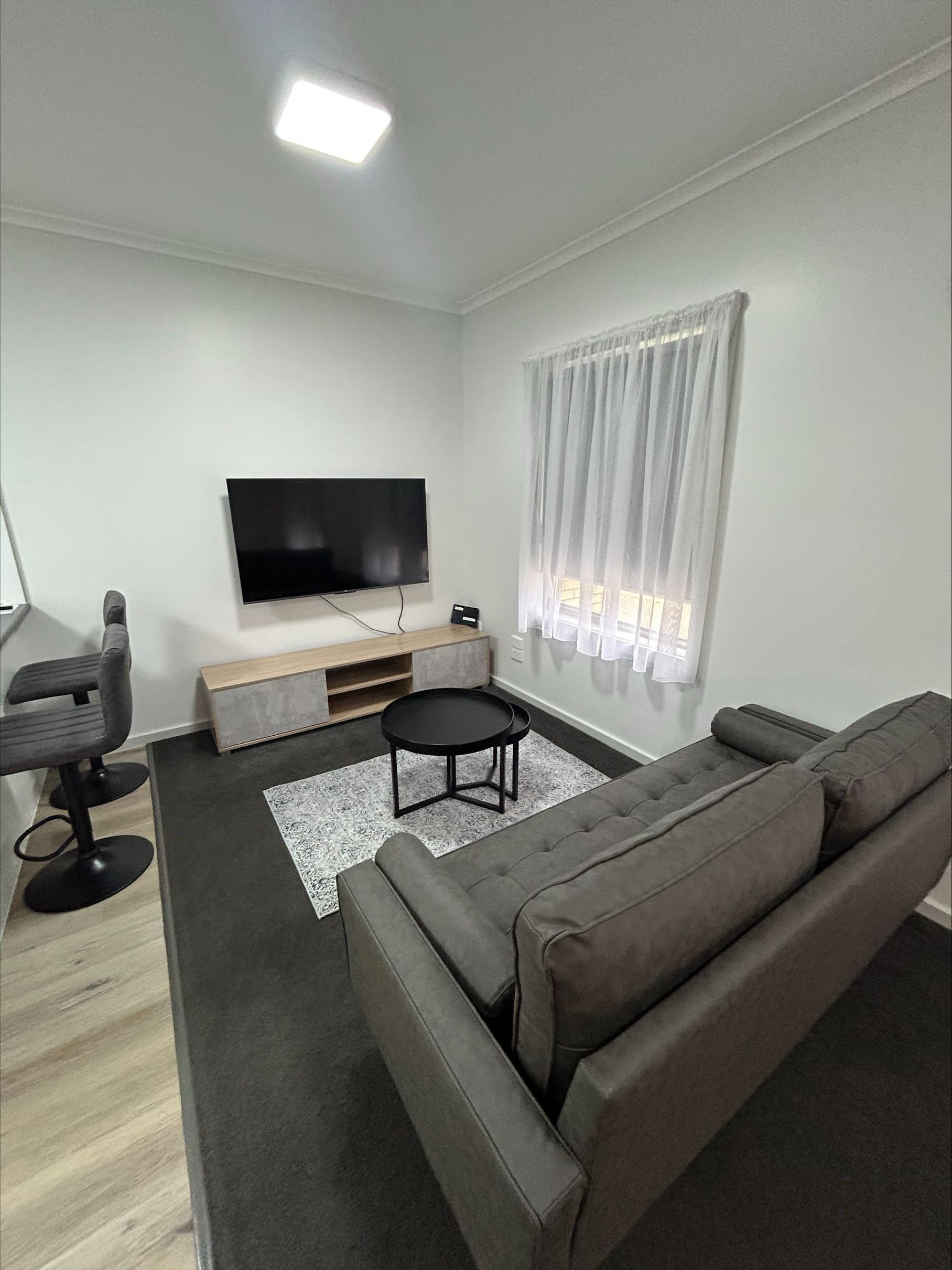 Living room with gray sofa, TV, black rug, round coffee table, and window with sheer curtains.