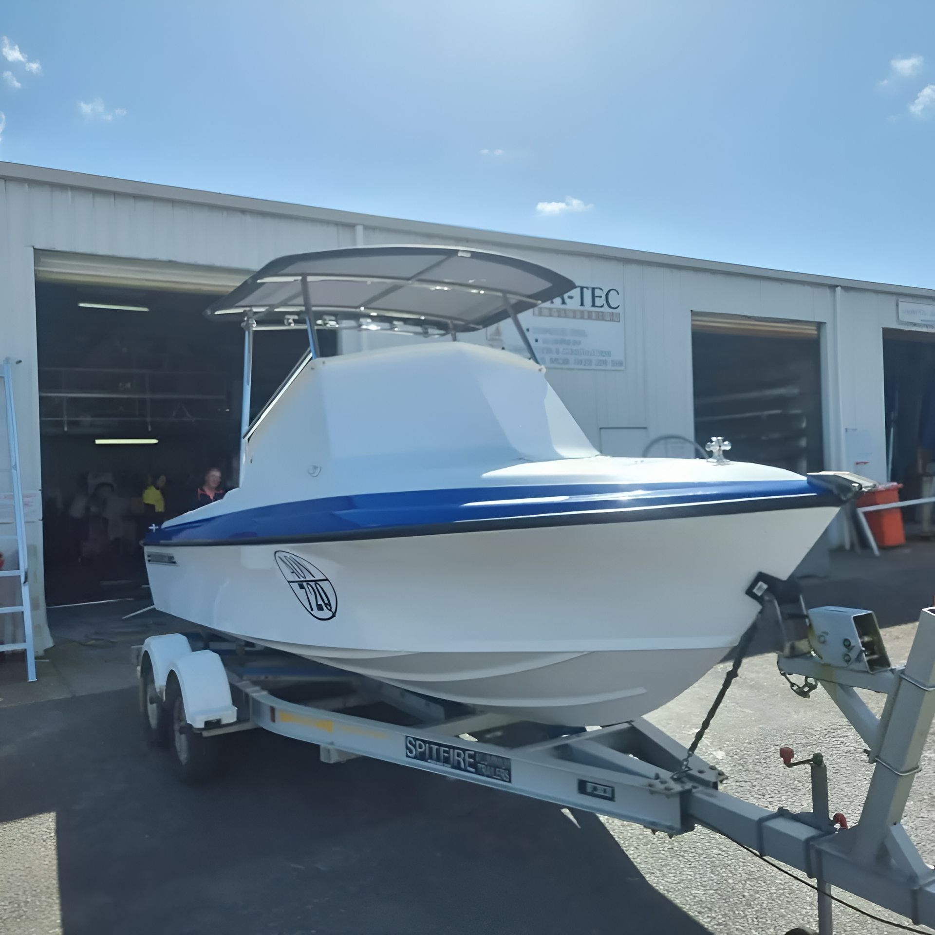 White and Blue Boat on a Trailer, Parked in Front of a Building — The Boat Cover Company In Buddina, QLD
