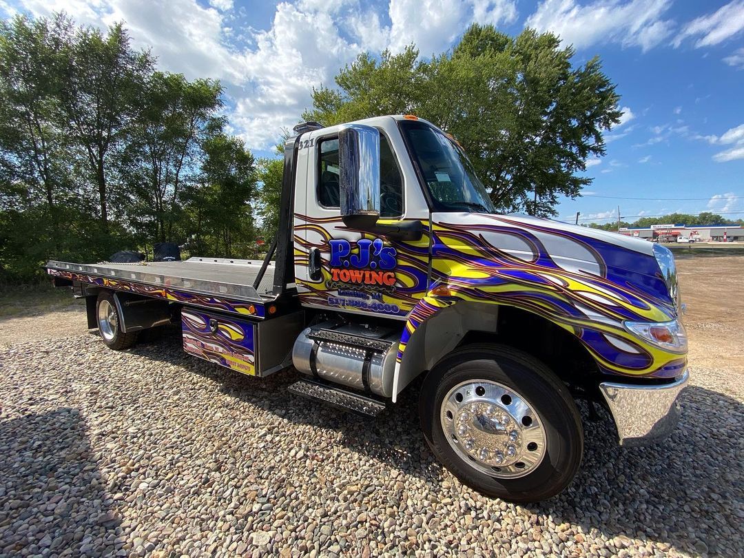 A colorful tow truck is parked in a gravel lot.
