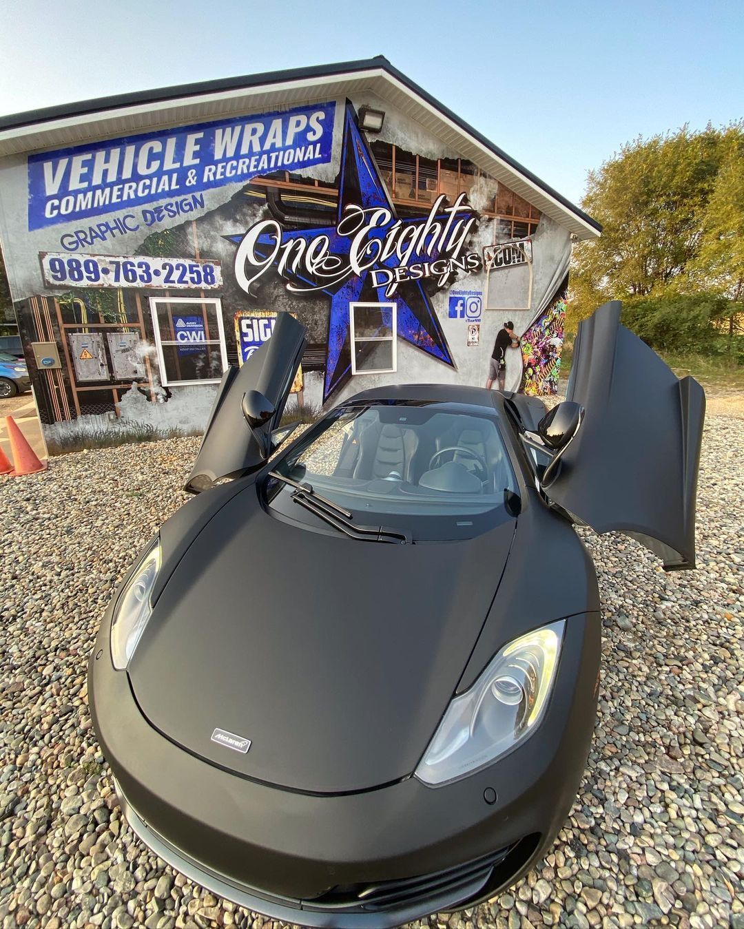 A black sports car is parked in front of a building with its doors open.