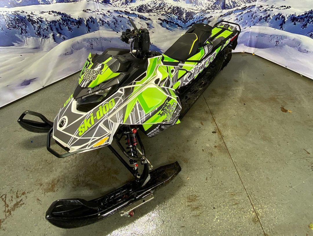 A green and black snowmobile is parked in a garage.