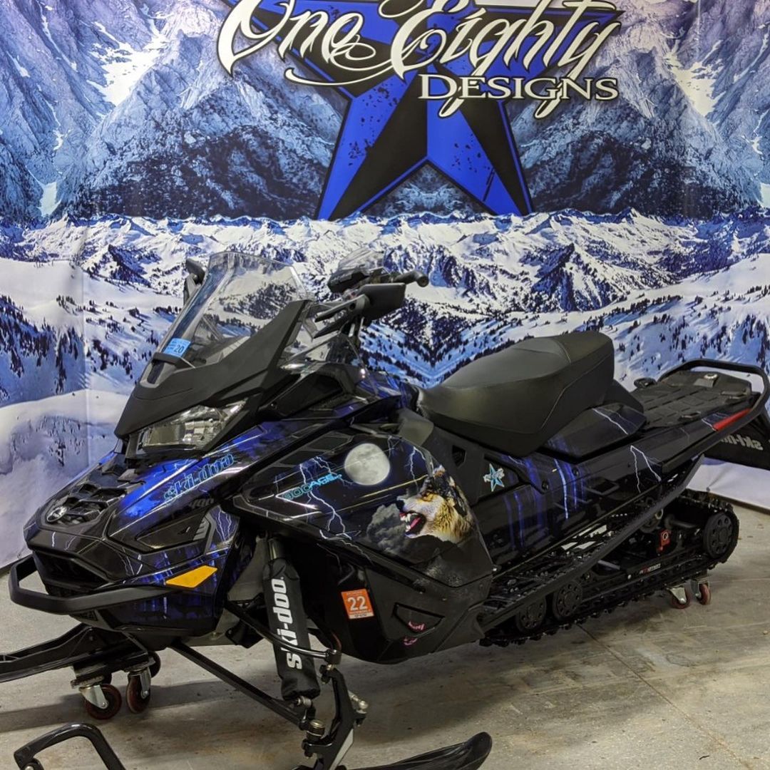 A snowmobile is parked in front of a sign that says one eighty designs