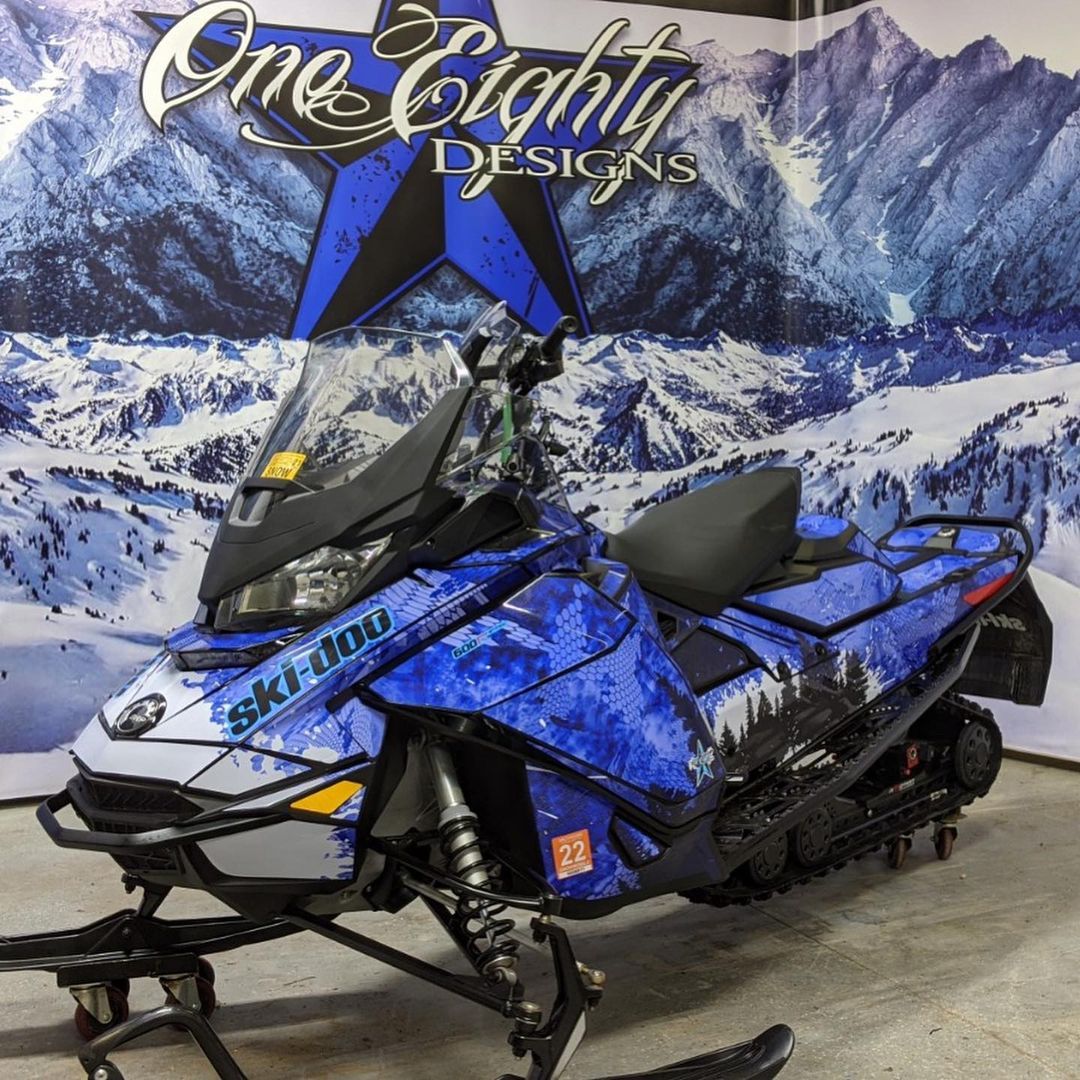 A blue ski doo snowmobile is parked in front of a sign that says one eighty designs