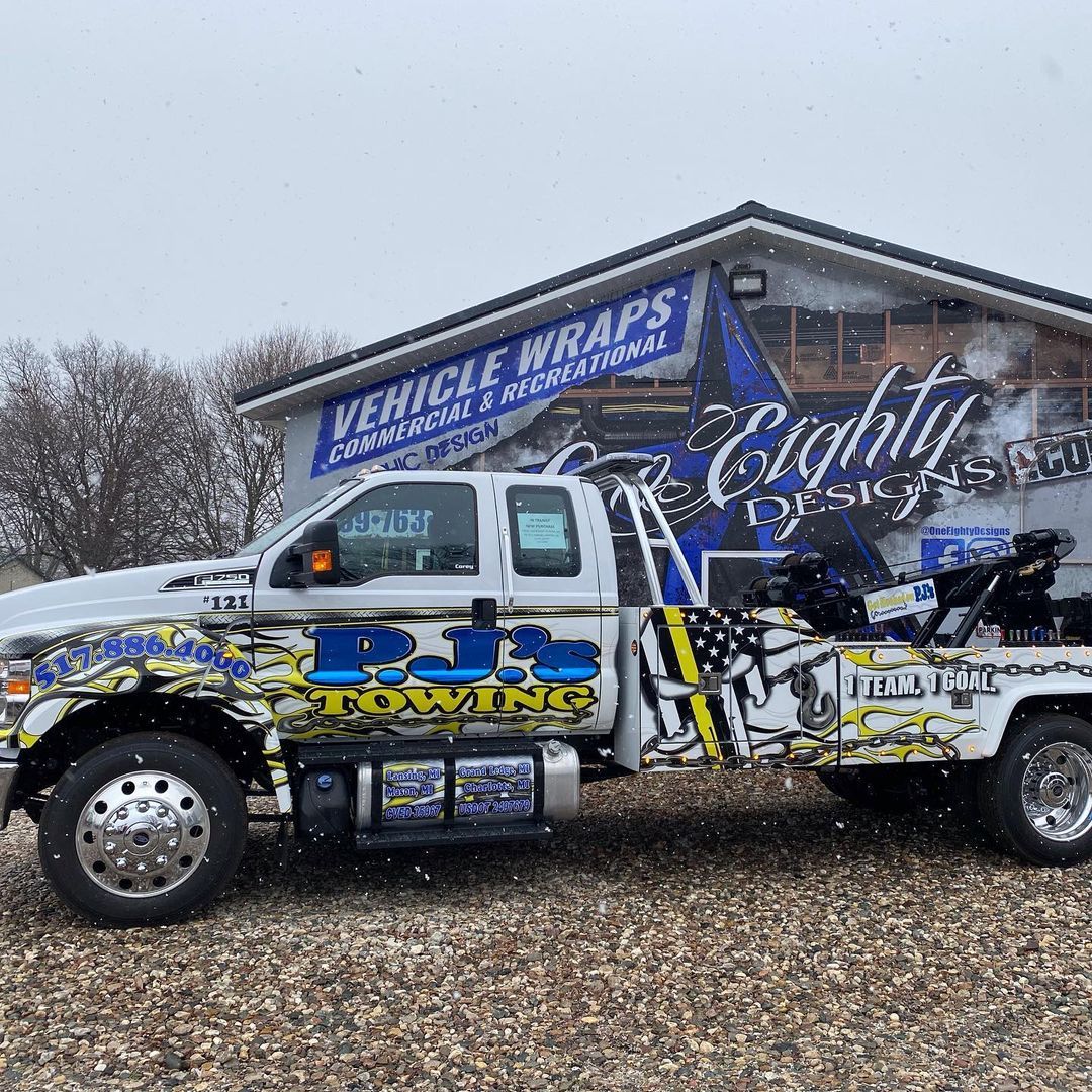 A tow truck is parked in front of a building that says vehicle wraps.