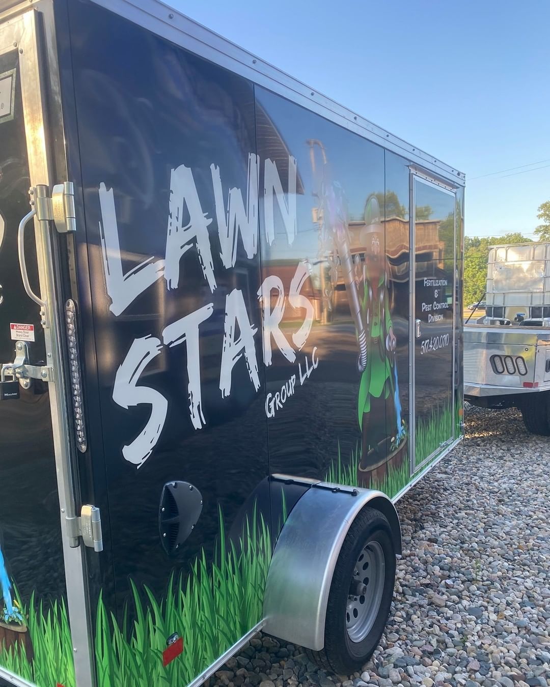 A trailer with a lawn stars logo on it is parked in a gravel lot.