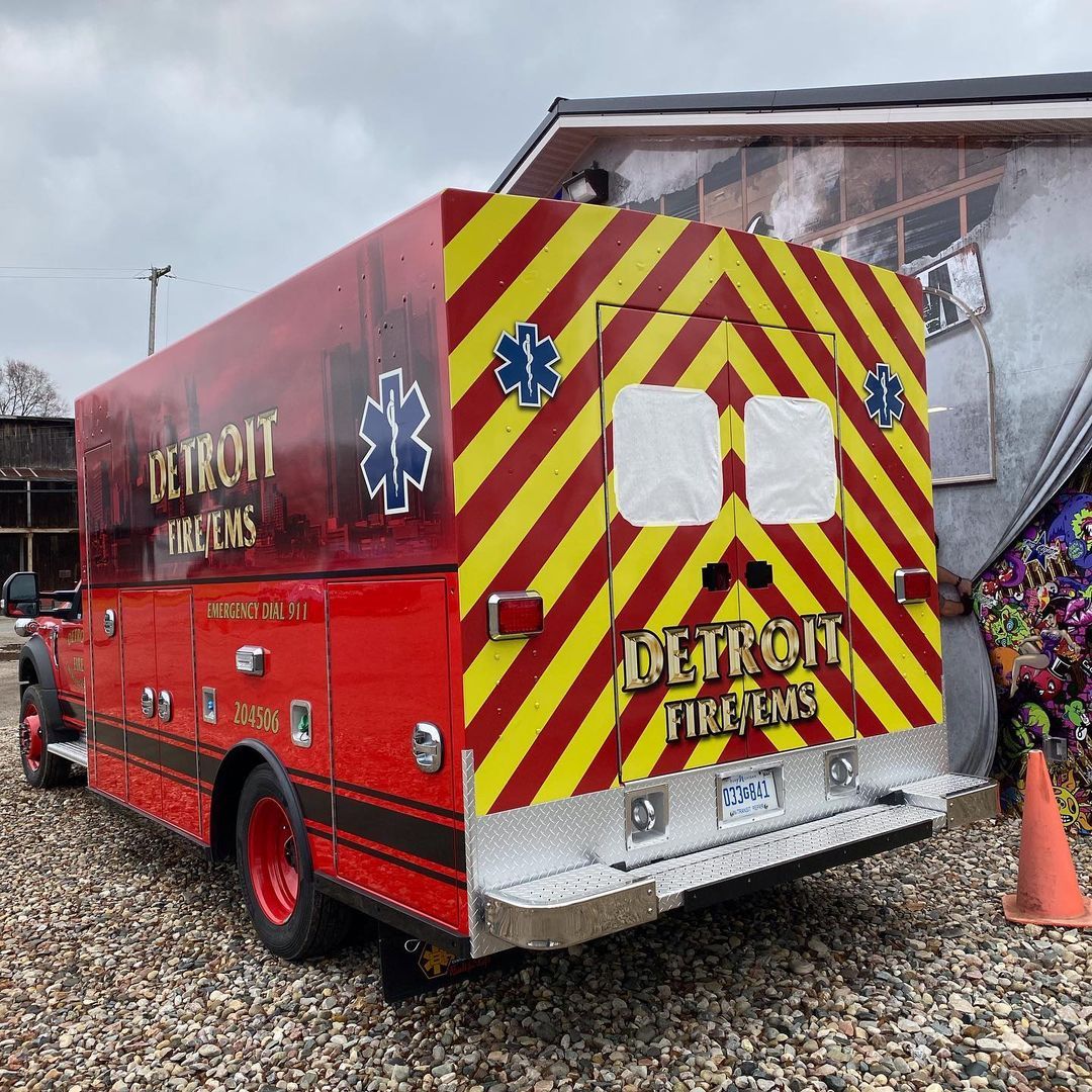 A red and yellow ambulance is parked in a gravel lot.