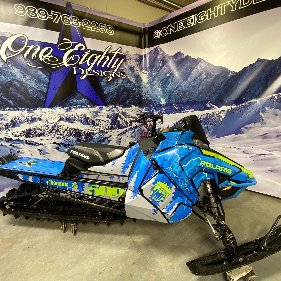 A blue snowmobile is parked in front of a sign that says one eighty.