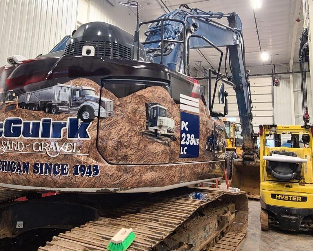 A large excavator is sitting in a garage next to a yellow forklift.