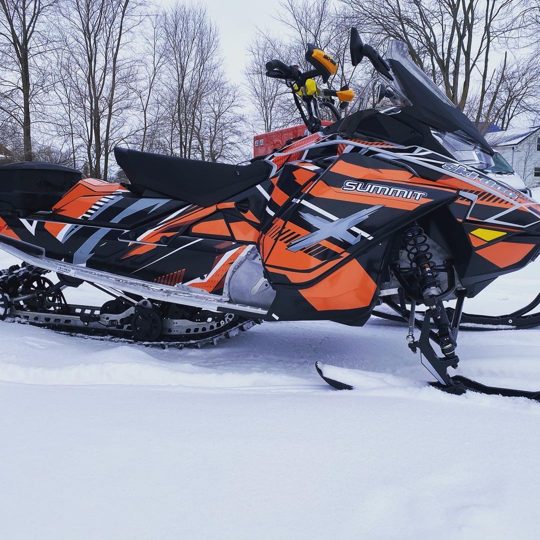 An orange and black snowmobile is parked in the snow