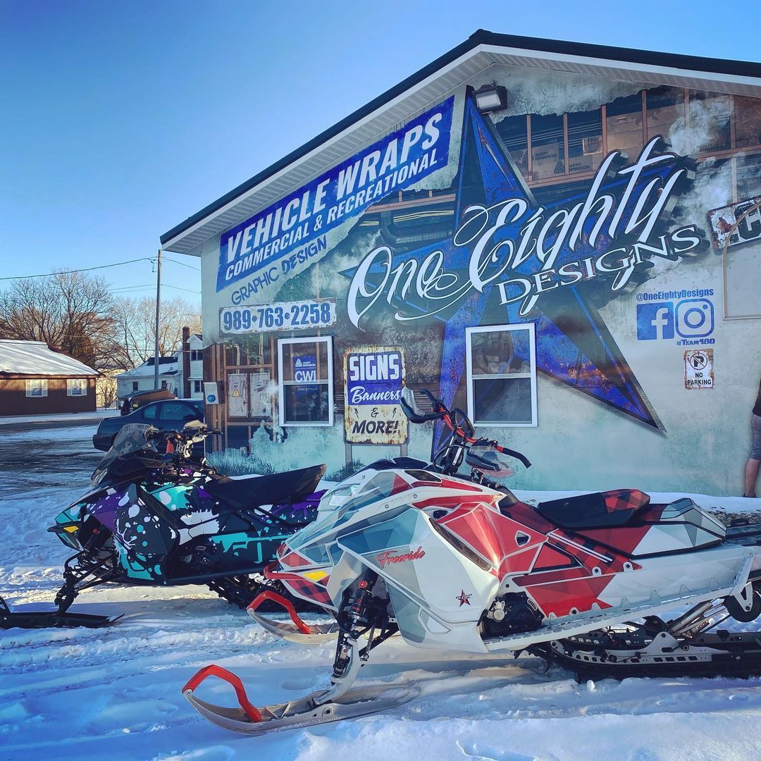 Two snowmobiles are parked in front of a building.