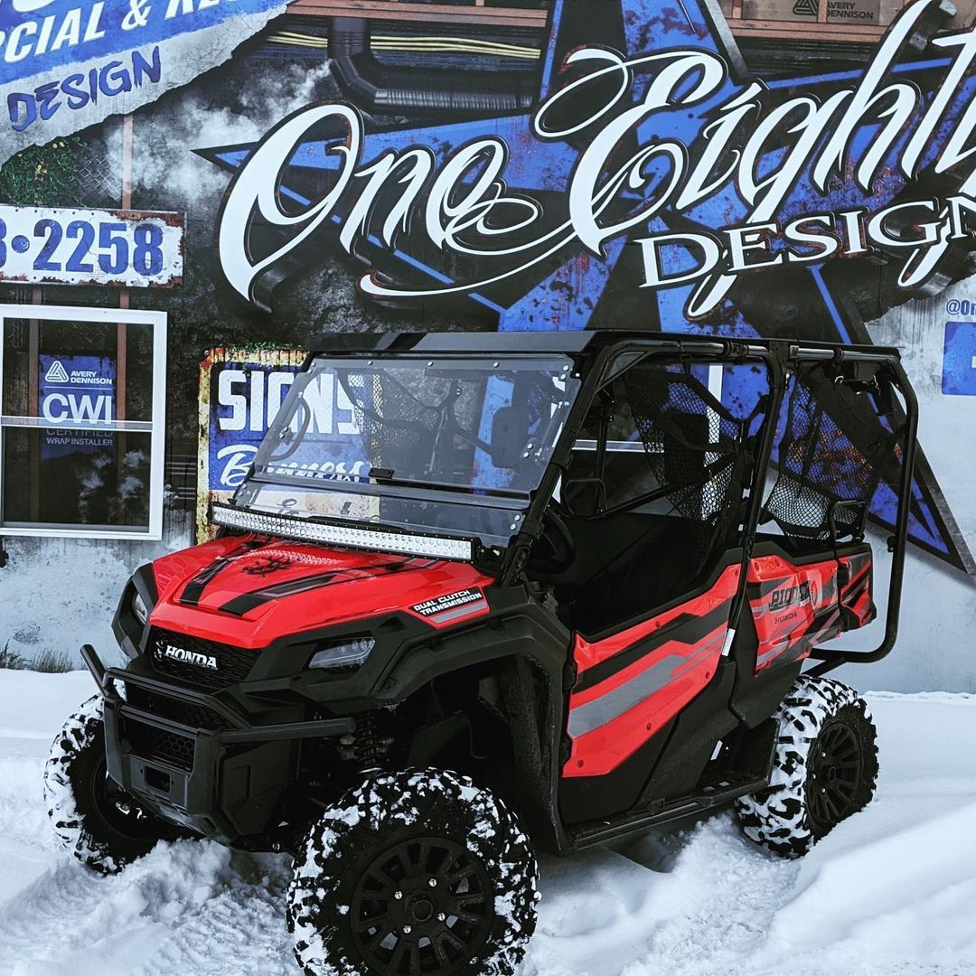 A red atv is parked in the snow in front of a one eight design sign.