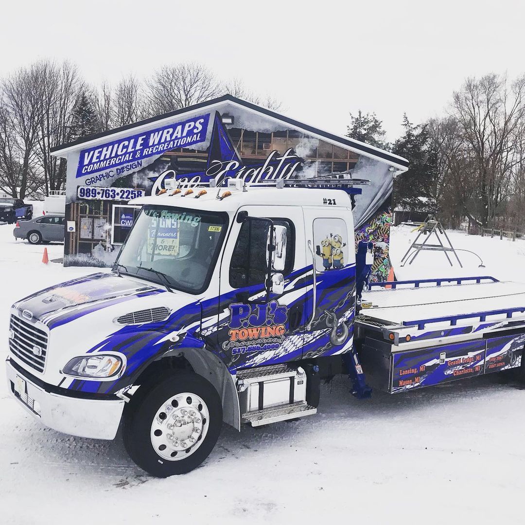 A blue and white tow truck is parked in the snow in front of a building.