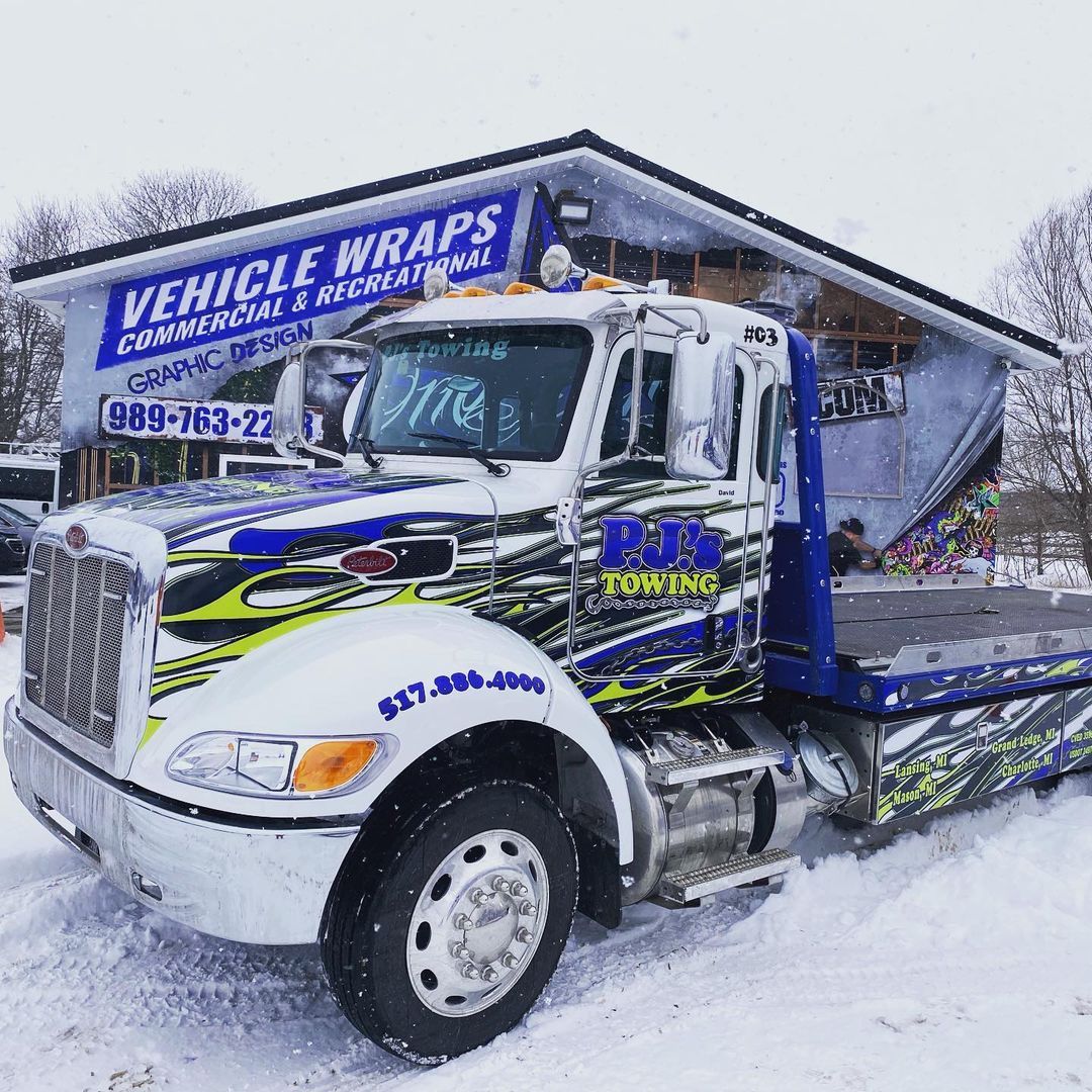 A tow truck is parked in the snow in front of a building.