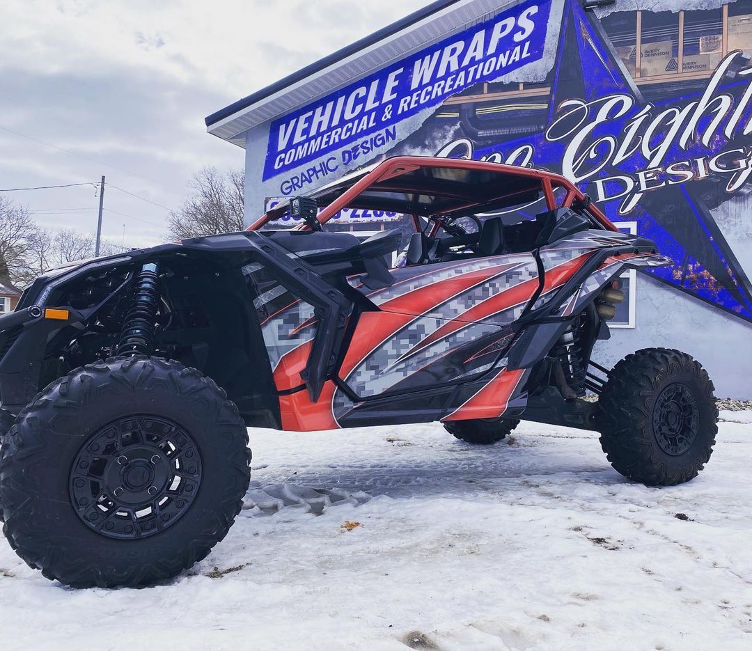 A red and black atv is parked in the snow in front of a building.