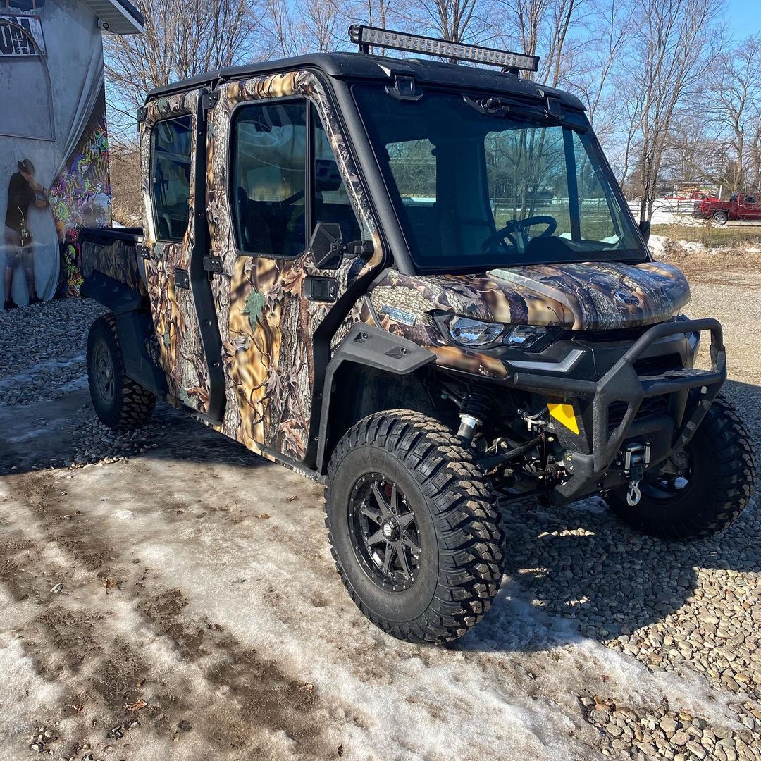 A camouflaged vehicle is parked in the snow in front of a building.