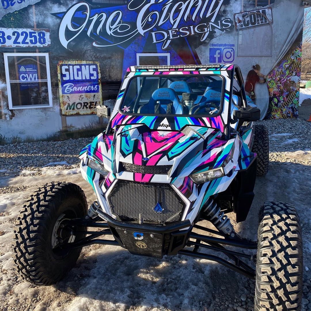 A colorful atv is parked in front of a building that says one origin designs