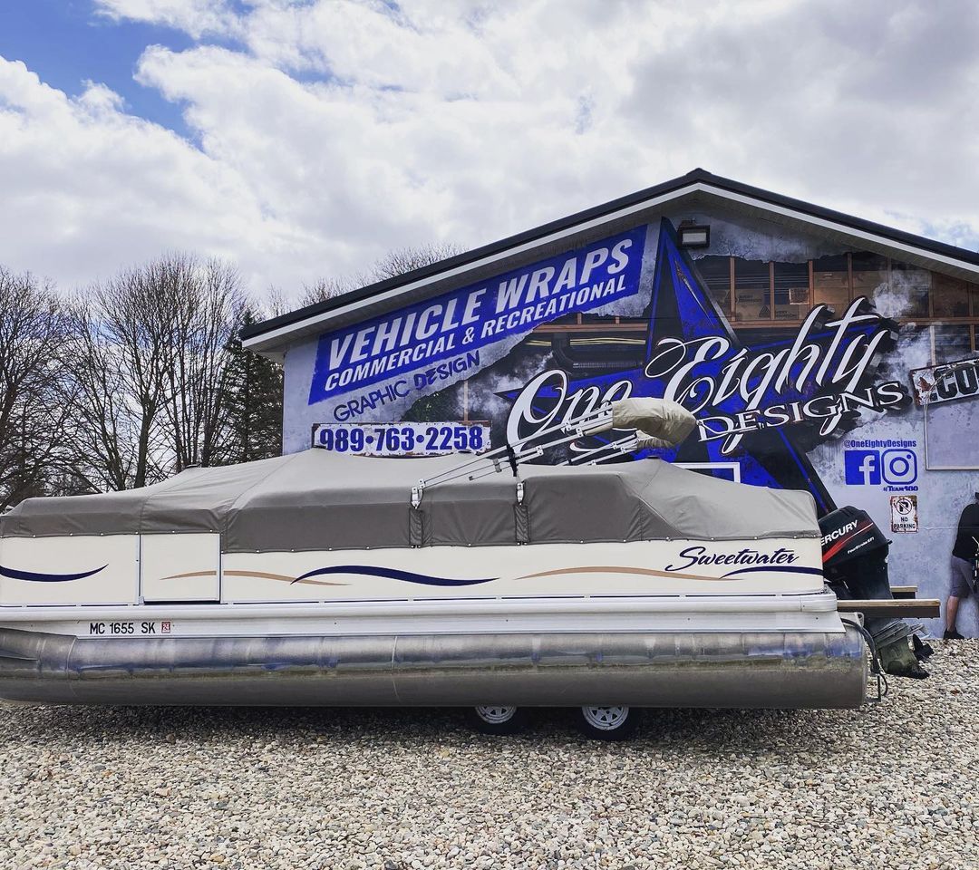 A pontoon boat is parked in front of a building that says vehicle wraps.