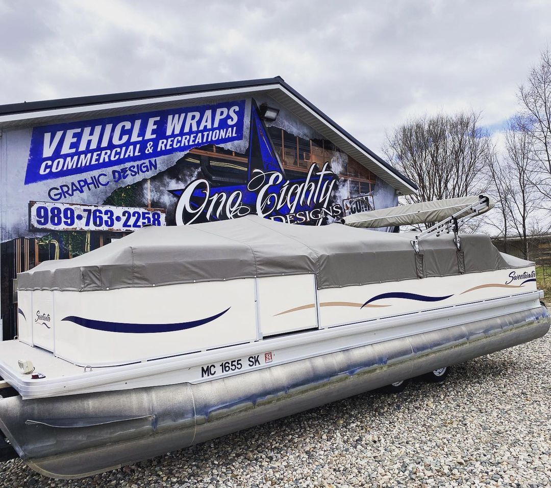 A pontoon boat is parked in front of a building that says vehicle wraps.