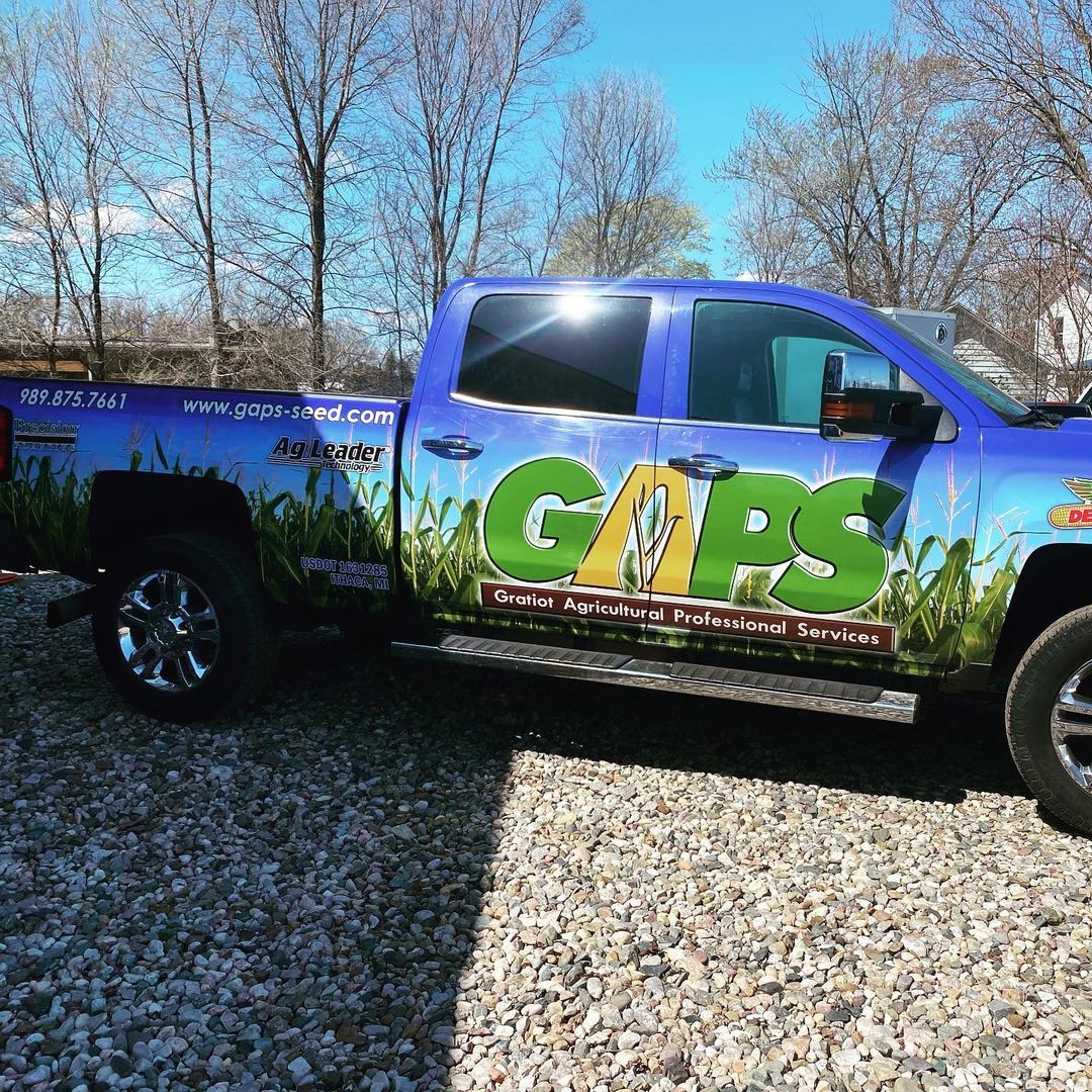 A blue truck with the word gaps on the side is parked in a gravel lot.