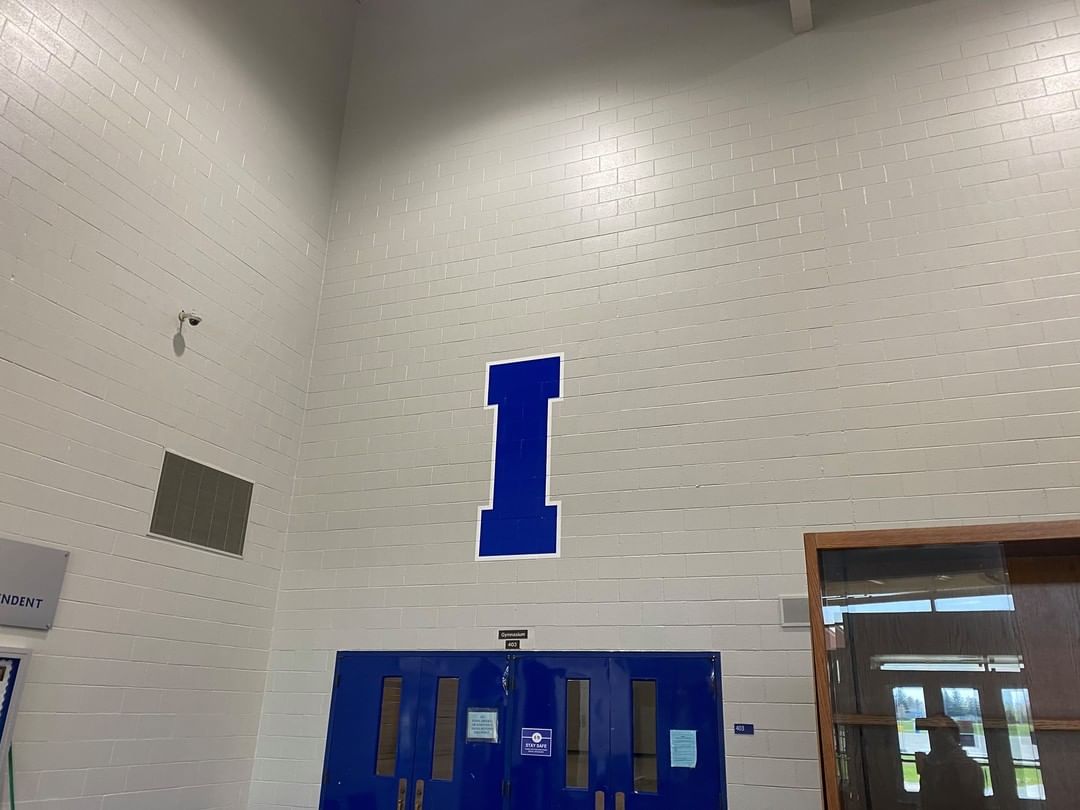 A blue letter i is painted on a white wall next to a blue door.