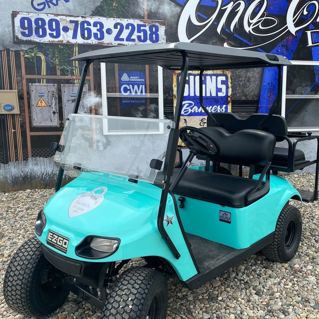 A blue golf cart is parked in a gravel lot in front of a store.