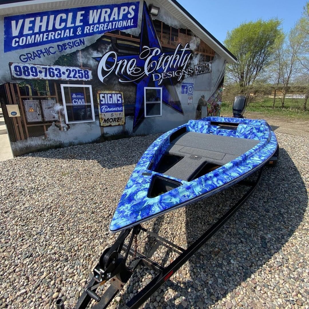 A blue boat is parked in front of a building that says vehicle wraps