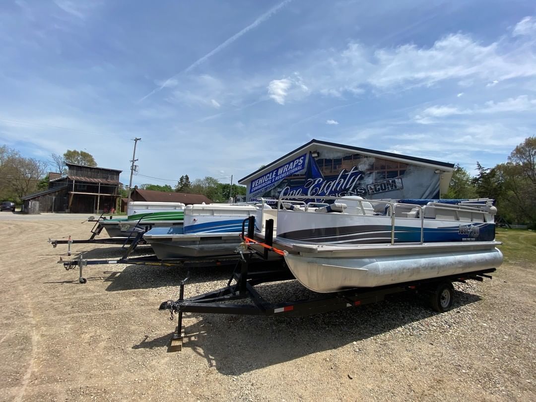 A row of pontoon boats are parked in a gravel lot.