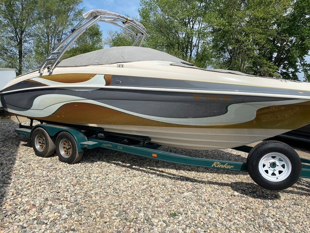 A boat is sitting on a trailer on a gravel road.