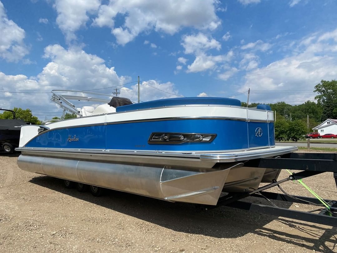 A blue and white pontoon boat is parked on a trailer.